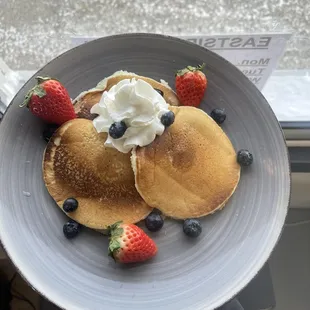 a plate of pancakes with whipped cream and berries