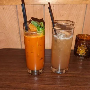 2 drinks, a candle, a napkin dispenser, and a table with a lovely wood paneled wall.