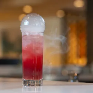 a red drink with ice and smoke
