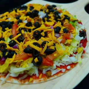 a pizza topped with cheese, black olives, lettuce, and tomatoes