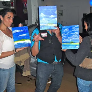  three people holding paintings