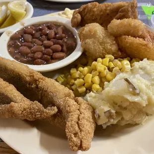 a plate of fried fish, mashed potatoes, corn, and beans