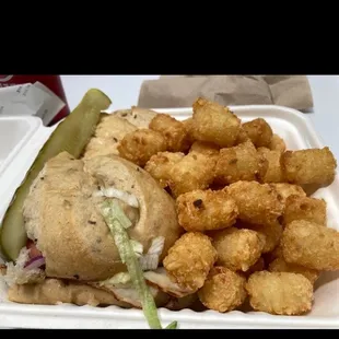 a sandwich and tater tots in a styrofoam container