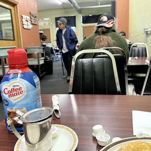 a table with a plate of pancakes and a bottle of coffee