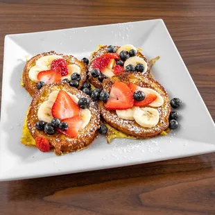 a plate of french toast with strawberries, blueberries and bananas