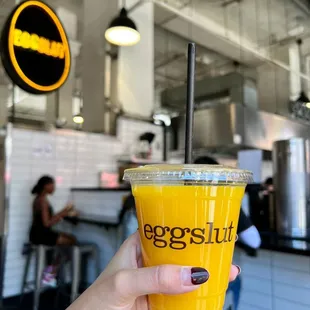 a hand holding a cup of orange juice