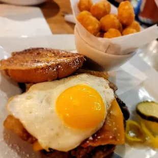 a fried egg on a toasted bun with a side of pickles