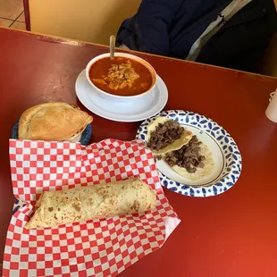 a table with a bowl of soup, burritos, and a plate of bread