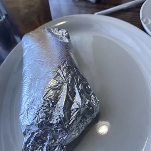 a burrito wrapped in foil on a plate