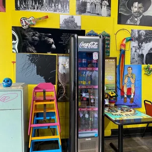 a yellow wall with pictures and a refrigerator