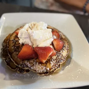 a stack of pancakes topped with whipped cream and strawberries