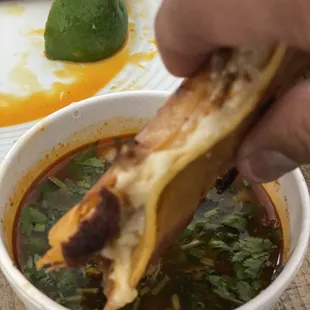 a person dipping a piece of bread into a bowl of soup