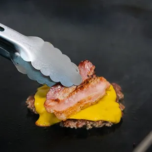 a bacon and cheese sandwich being cut with a knife