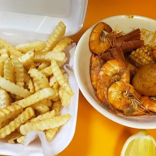 a bowl of shrimp, fries, and lemon wedges