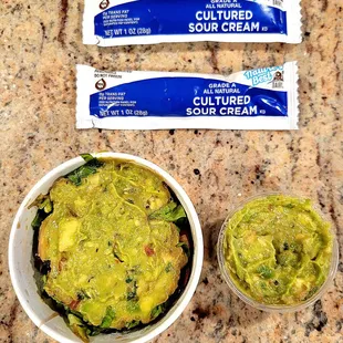Guacamole with lettuce, tomatoes, olives, and cilantro on the left. Fresh guacamole on the right. Sour cream packets above.