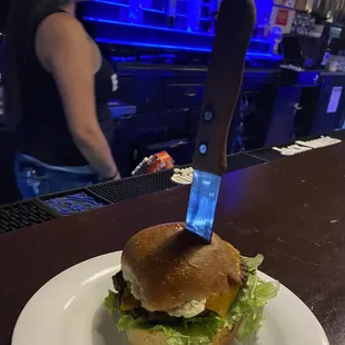 a burger on a plate with a knife sticking out of it
