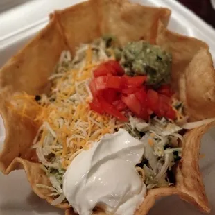 Taco salad with beef, guacamole, sour cream, lettuce, tomato, cheese, onion, cilantro, refried beans.