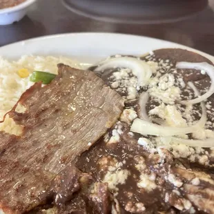 Enfrijolada: hand-made tortillas w/Blk Bean sauce, topped w/thinly-sliced raw onions; rice, thin slice of marinated beef steak