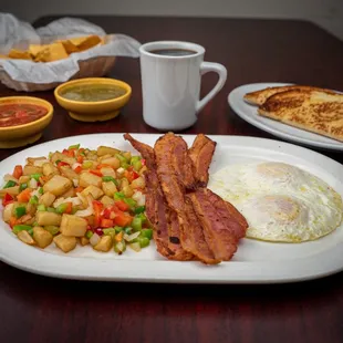 The meal consists of three bacon slices, two fried eggs, and potatoes mixed with bell pepper and onion. A side of white toast is also includ