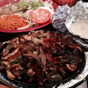 Chicken and steak fajitas with peppers and onions retried beans lettuce sour cream and guacamole.