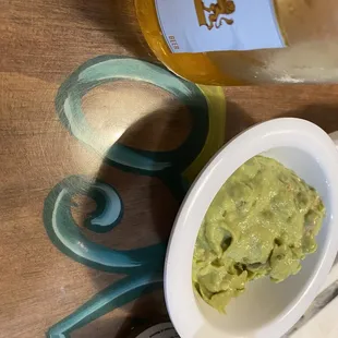 a bowl of guacamole next to a bottle of beer
