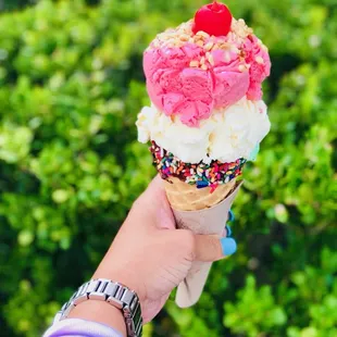 a hand holding an ice cream cone with sprinkles and a cherry