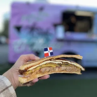 a person holding a sandwich in front of a food truck