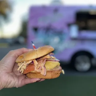 a person holding a sandwich in front of a food truck