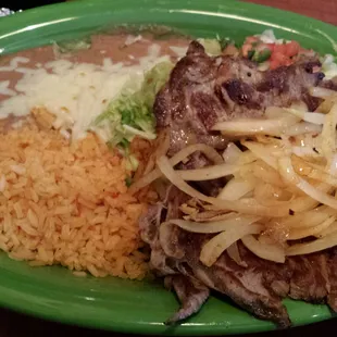 Steak Tampequeño.. Ribeye topped with grilled onions, refried beans with cheese, salad with Pico de Gallo &amp; guacamole
