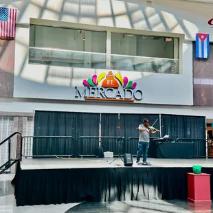 The entrance and a stage with a man playing a violin entertaining people sitting and walking by.