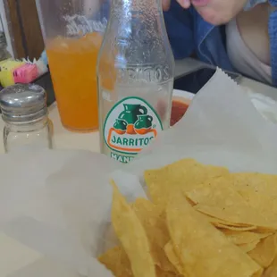 a child sitting at a table with chips and a bottle