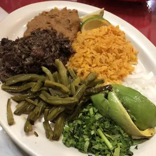 Barbacoa Plate with limes, rice, cactus, refried beans, avocado, onions, and cilantro - Delicious