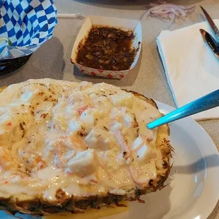 A half a Pineapple filled with a variety of seafood and a super sauce all covered in cheese.