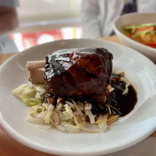 Chamorro - Bone-in pork shank slow cooked in brine for 24-hours. Thick, tangy ancho-pasilla piloncillo sauce. spicy slaw.