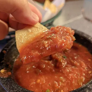 a person dipping a tortilla into a bowl of salsa