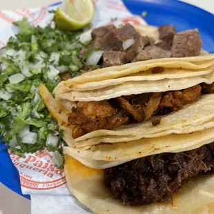 Barbacoa (slow-cooked, shredded beef), Pastor (pork), y Lengua (beef tongue) tacos con tortillas de maize (corn)