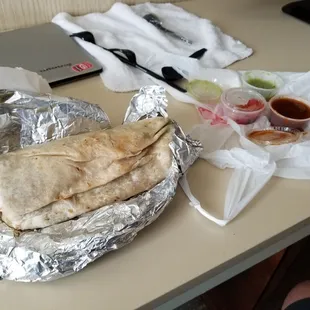 Shrimp burrito, with various hot sauces and fresh chips.