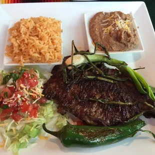 Carne asada with small amount of rice and beans. Also  lettuce, few cheese shreds, and tomatoes piled together.