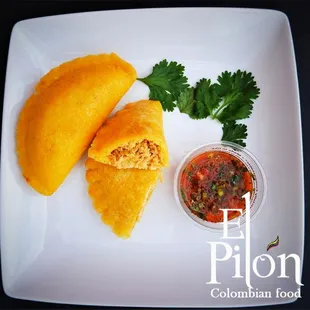 A pair of chicken empanadas with Aji on the side.