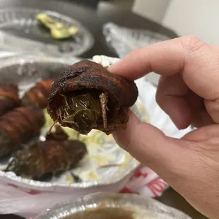 a hand holding a piece of bacon wrapped in onions