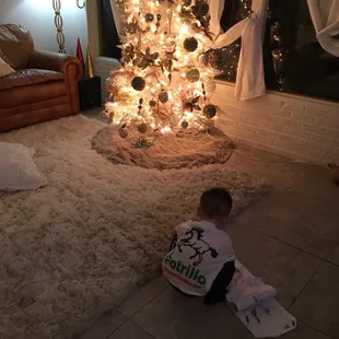 a little boy sitting in front of a christmas tree