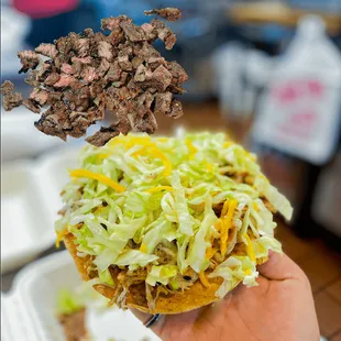 a hand holding a taco with shredded beef and lettuce