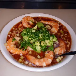 a bowl of soup with shrimp and avocado