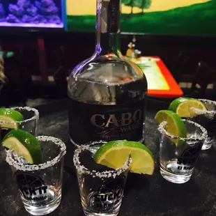 three shot glasses with limes and a bottle