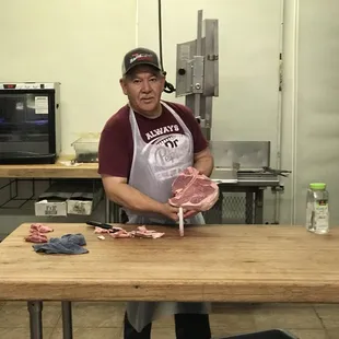 a man in a red shirt and white apron holding a piece of meat