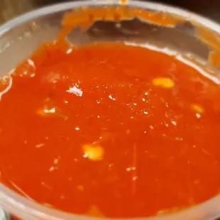 a bowl of sauce with a slice of bread in the background