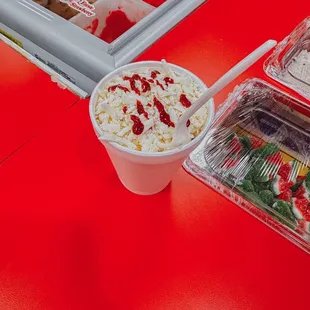 a red table with a plastic container of food and a plastic container of ice cream