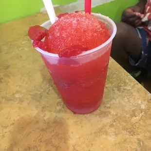 a red drink with strawberries in a plastic cup