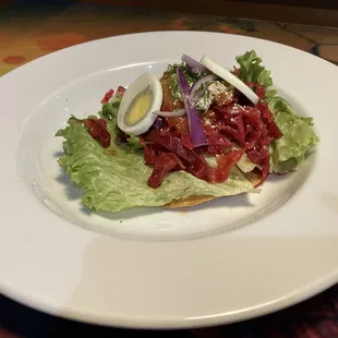 Enchilada Chapina (Tostada with cabbage and beet salad, ground beef, tomato sauce, boiled egg slices, cojita cheese, onion, and parsley)