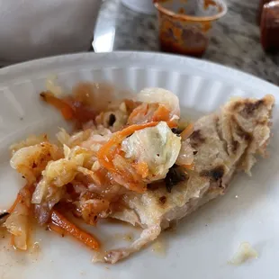 About 1/3 of a pupusa with curtido, the tomato sauce, and hot sauce.